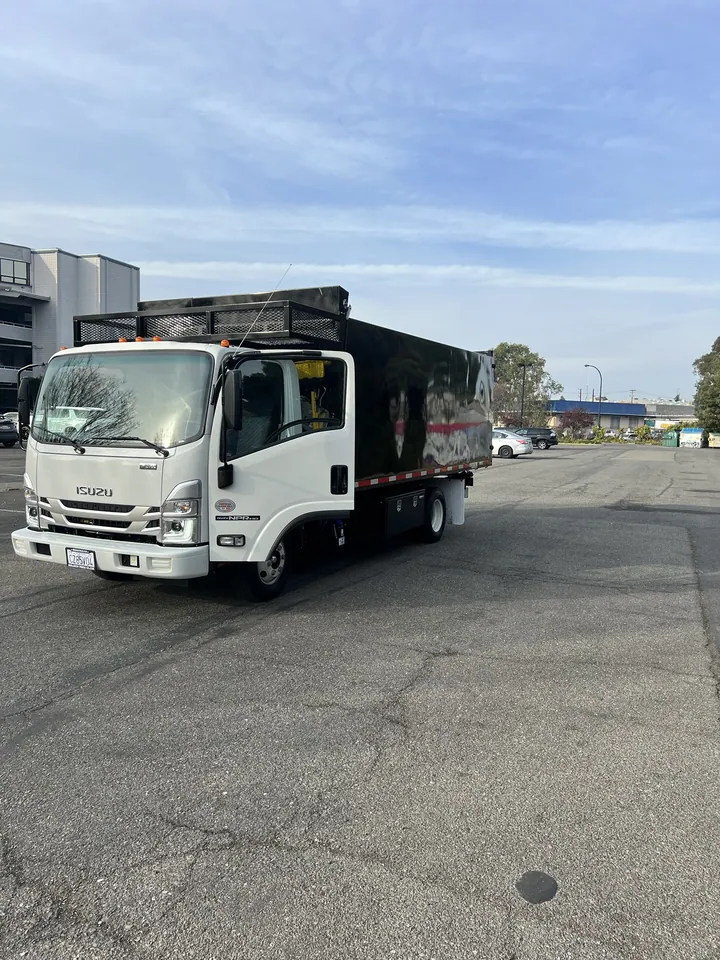 The Rainbow Junk Removal truck, a white Isuzu with a fourteen foot dump body and a loading ramp