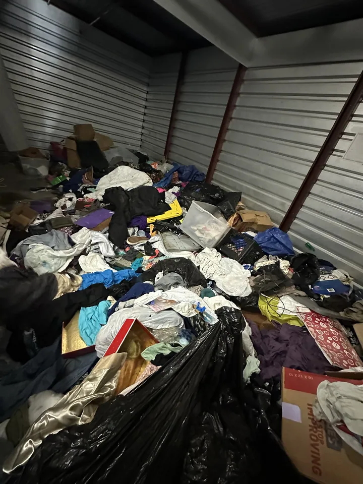 A storage unit filled to the back wall with bags, clothing and boxes